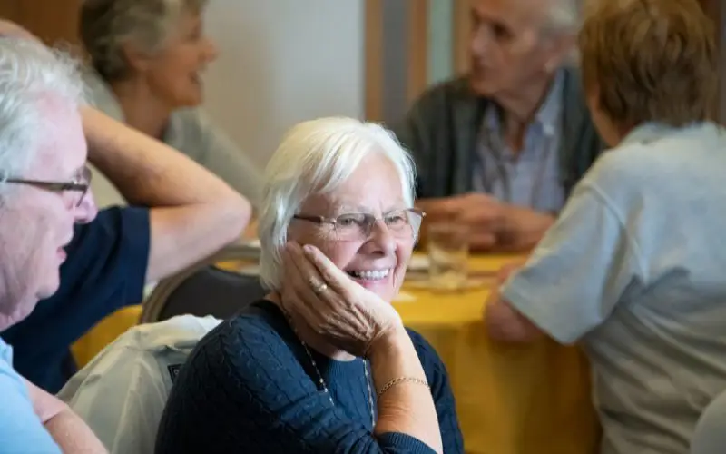 A woman smiles while in the company of others sat at her table. 