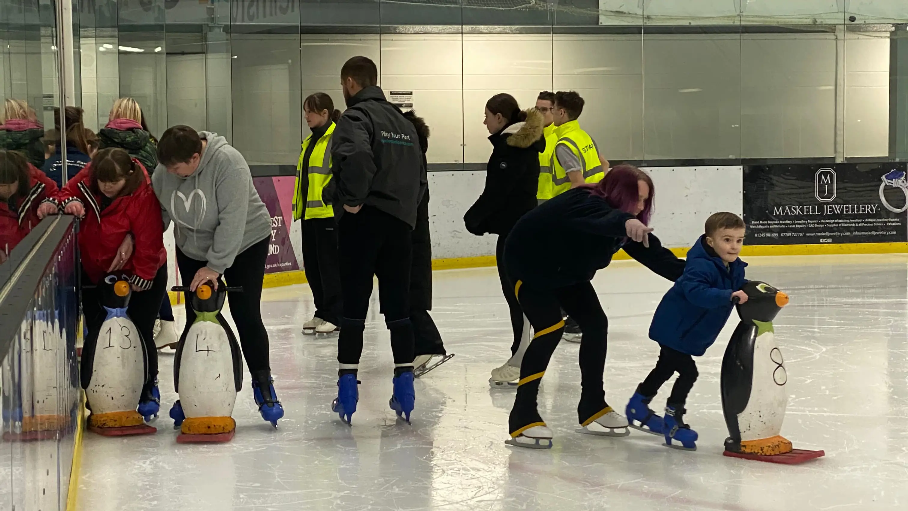 Group of young children learning to ice skate with penguin aids