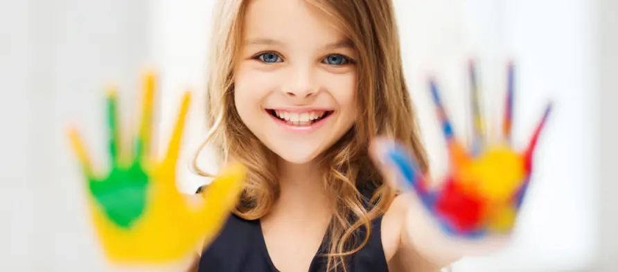 Smiling young girl holding up hands covered in bright paint
