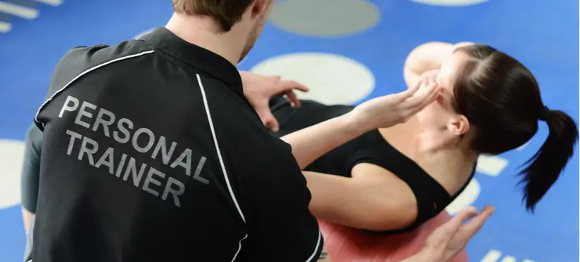 Man wearing t-shirt saying 'Personal trainer' helping women who is doing crunches on a exercise ball