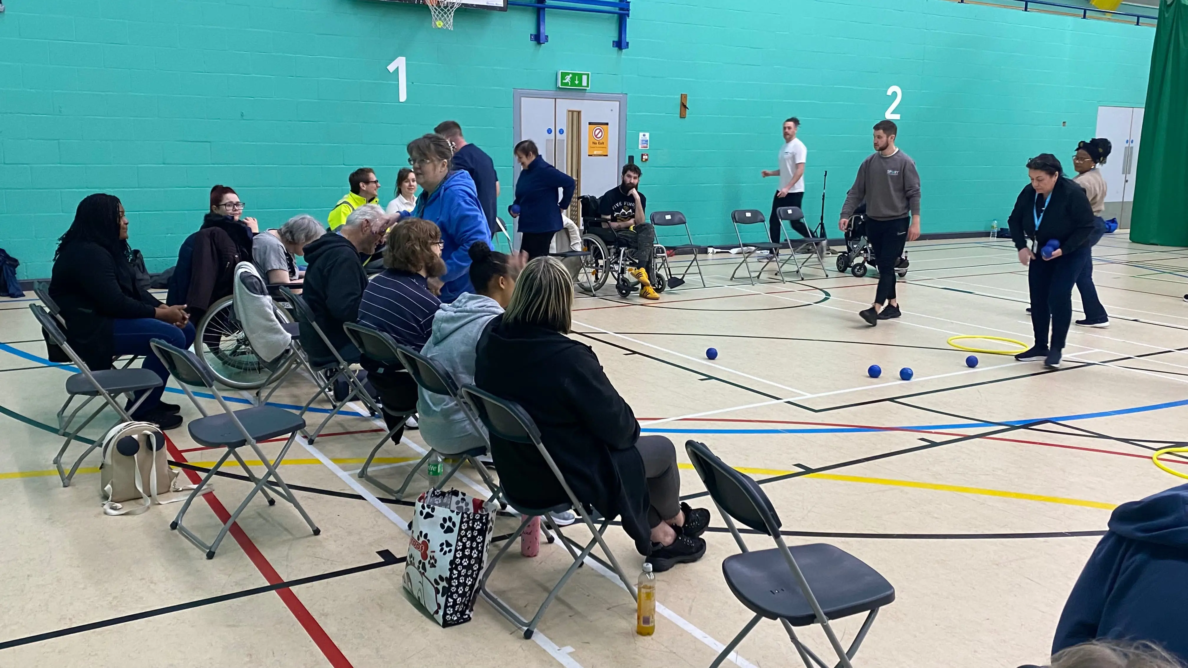 A group of people sat in a sports hall waiting for a game to be set up