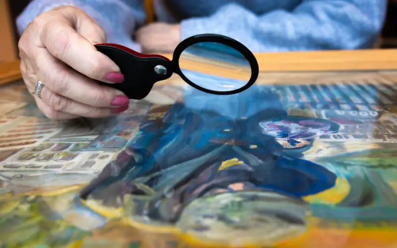 A close up of a woman looking at a painting with a magnifying glass. 