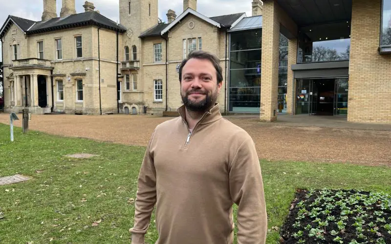 A man standing on the lawn outside Chelmsford Museum smiles at the camera. 