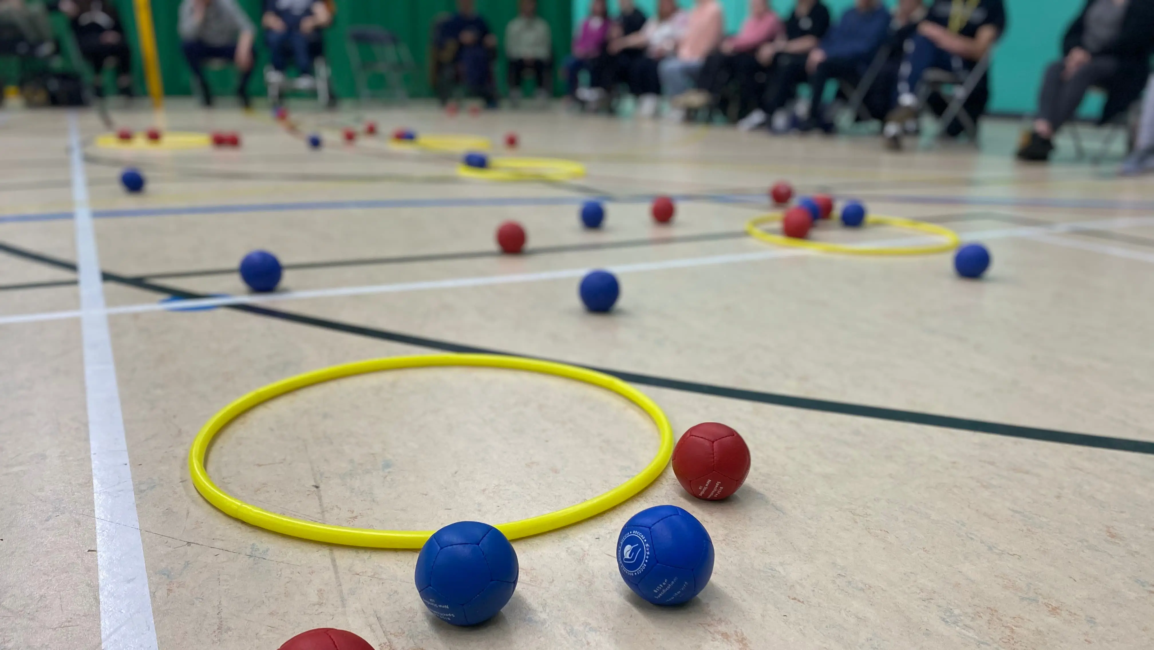 red and blue Boccia balls on the floor of a sports hall, next to a yellow hoop