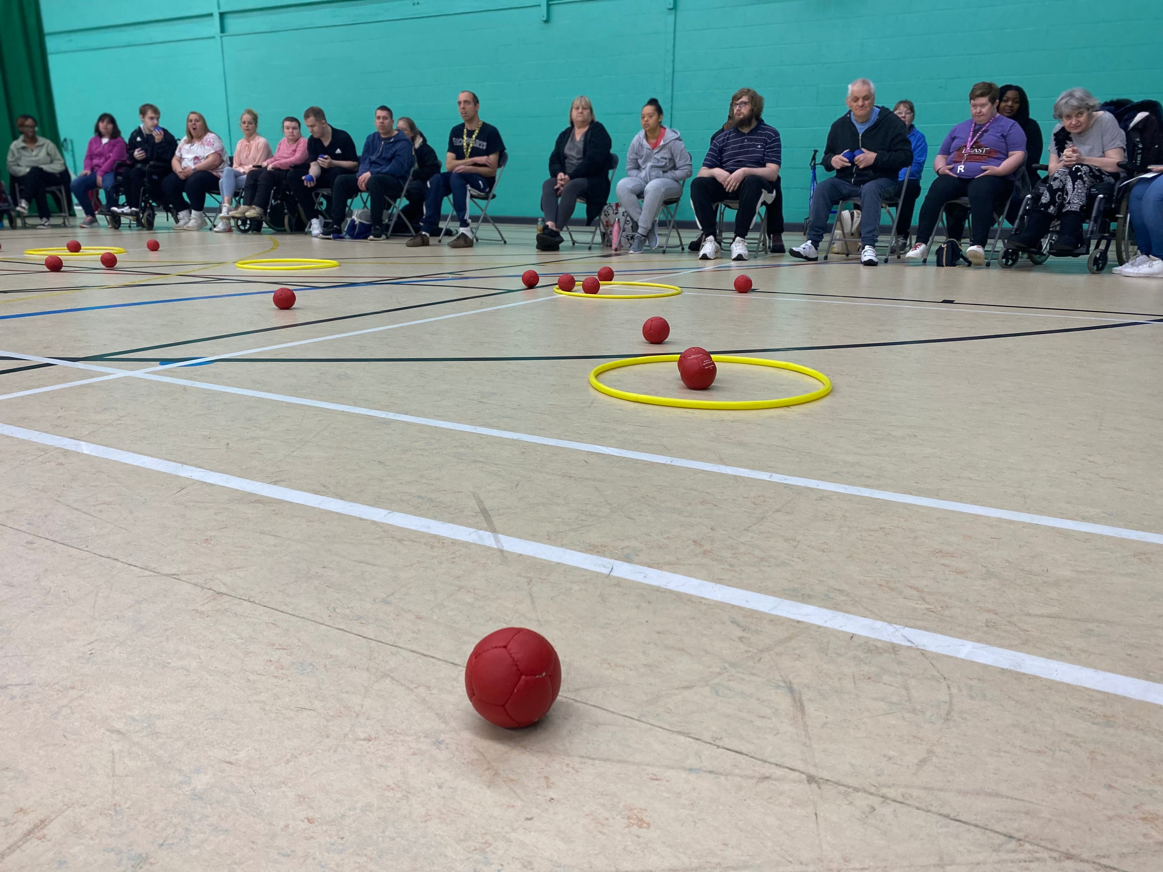 red Boccia balls on the floor of a sports hall next to a yellow hoop preview