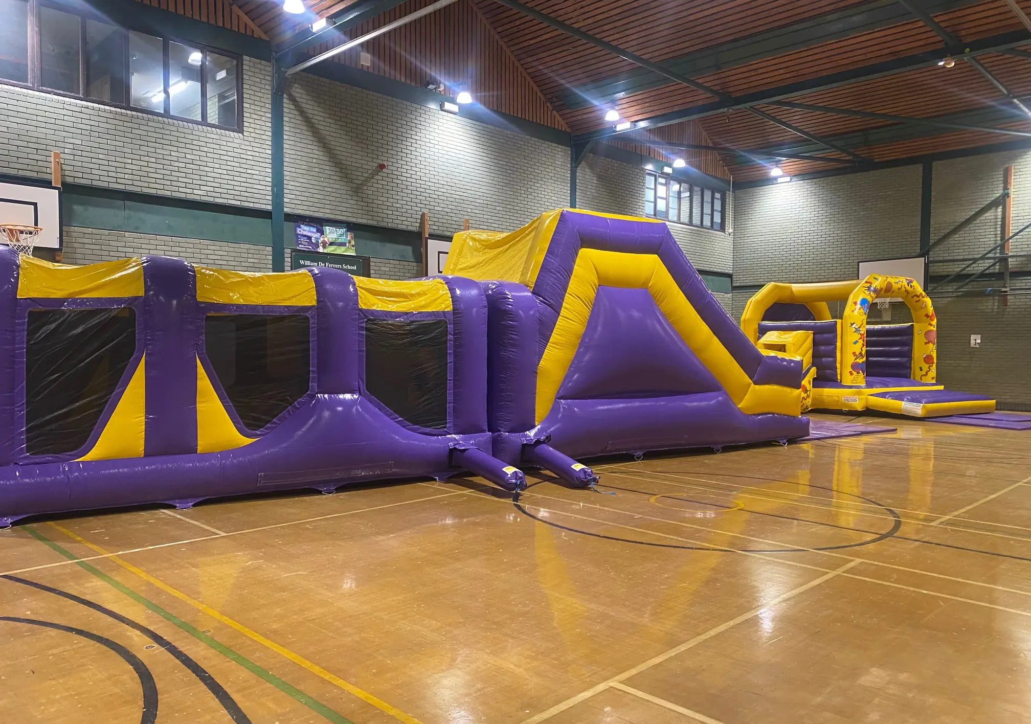 Large purple and yellow inflatable obstacle course and matching bouncy castle set up in sports hall