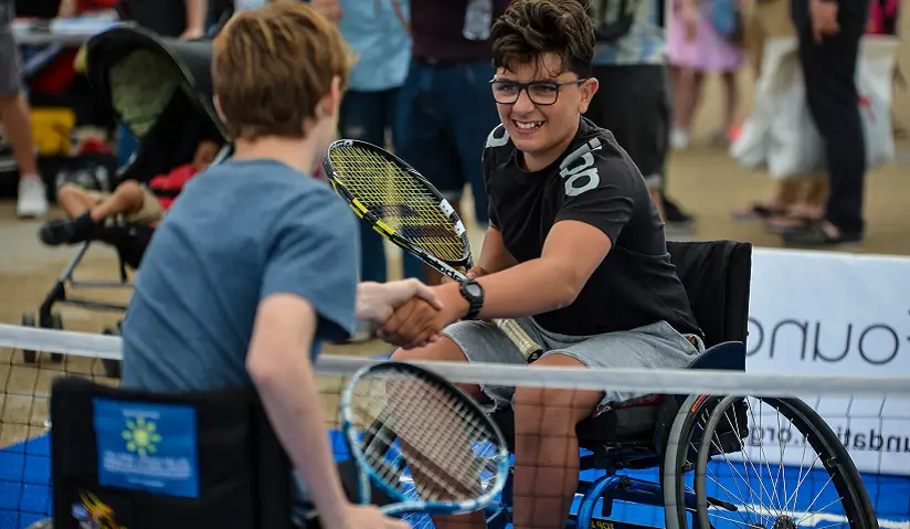 Two older boys in wheelchairs shaking hands over the net on a tennis court