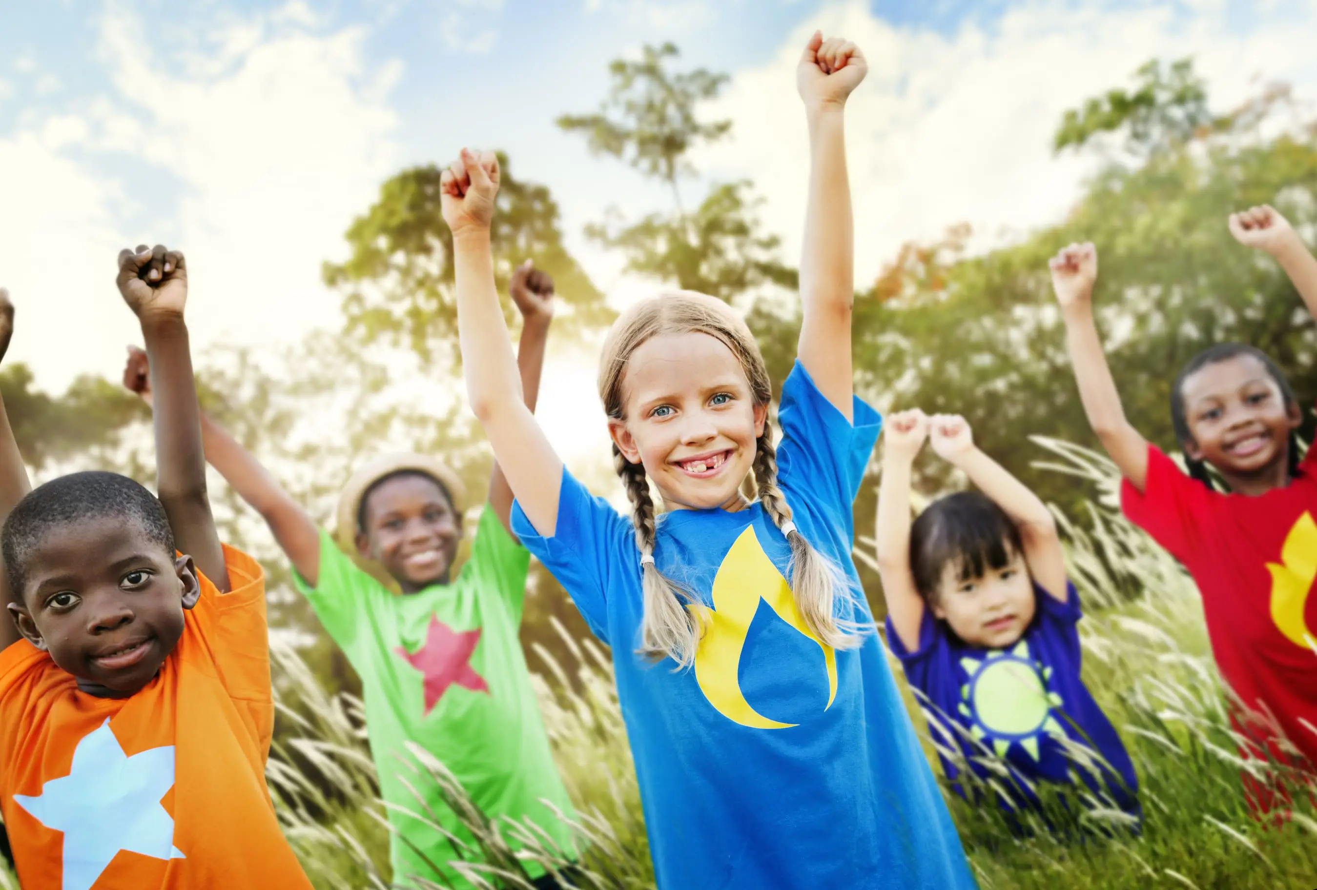 Group of happy young children smiling with their arms in the air, wearing brightly coloured t-shirts